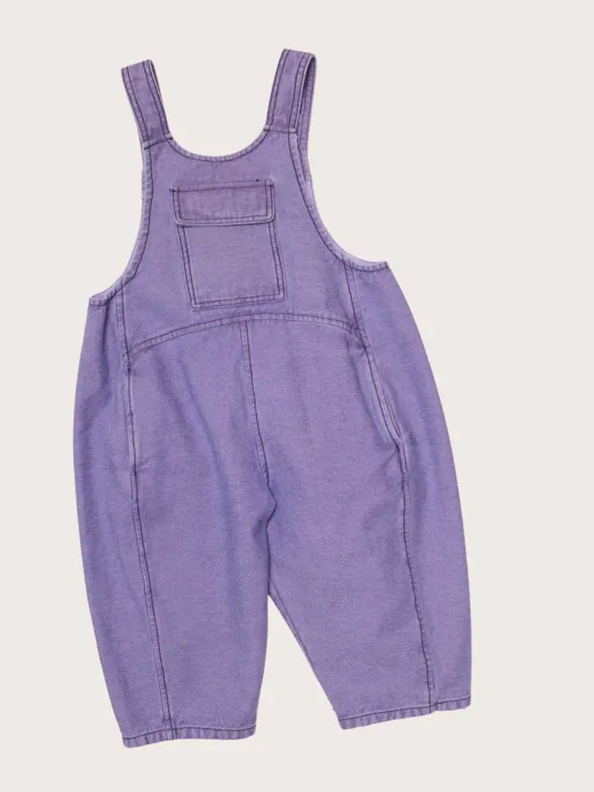 Front flat lay of Studio Koter Kai dungarees in Lilac Overdye, washed lilac denim with a chest patch pocket and button straps.