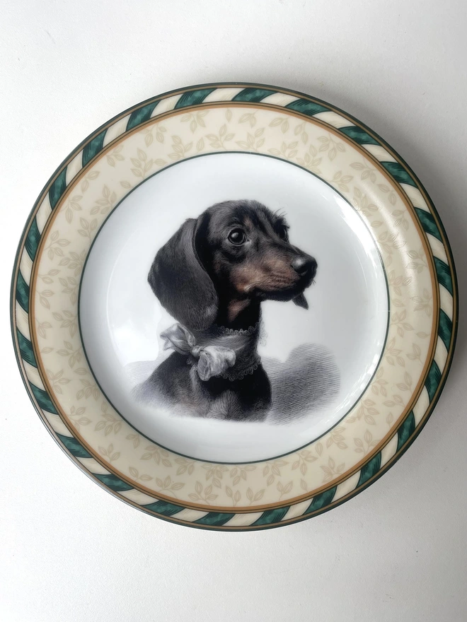 a vintage plate with an ornate border, in the centre of the plate is a vintage style black and white illustration of a beautiful dachshund dog puppy