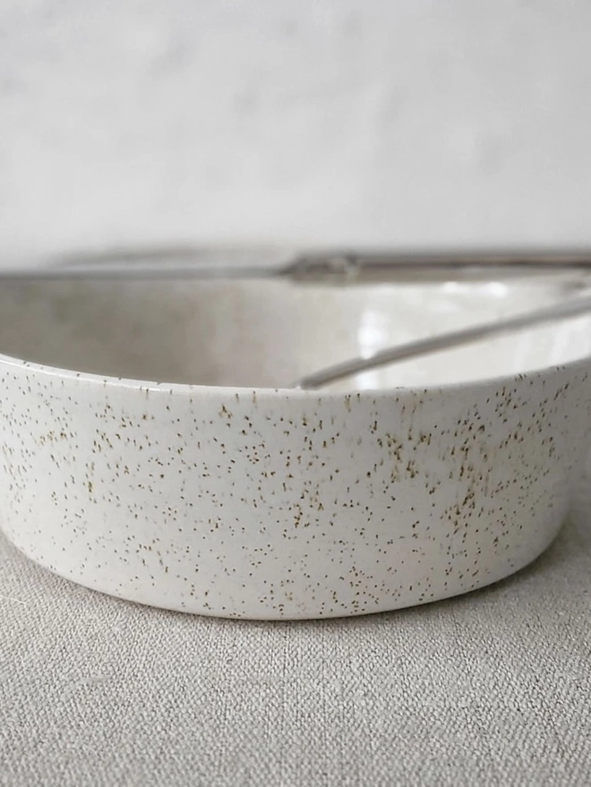 Classic Pasta Bowl, a colourful ceramic bowl sitting on a plain surface against a grey backdrop. It is accompanied by a spoon. 