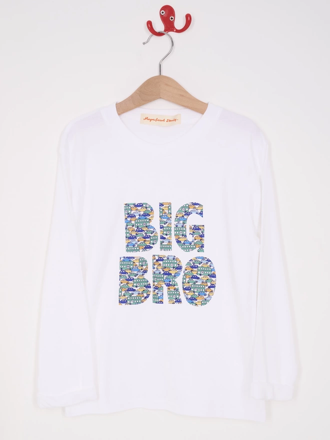 Big Bro appliquéd in a vintage cars Liberty print on a white cotton long sleeve t-shirt. Hanging on a hanger.