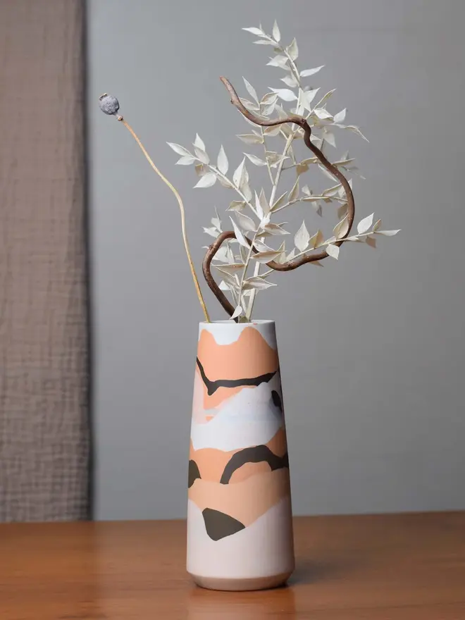 porcelain vase on table, vase has shades of orange, brown, and whites, and is holding dried foliage