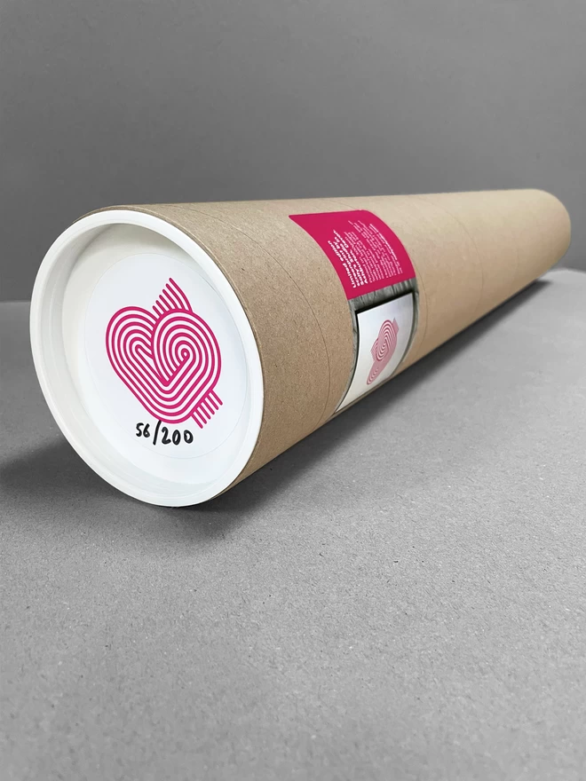 A cardboard tube laid on a plain grey background, containing the heart print with a sticker on the end depicting that.