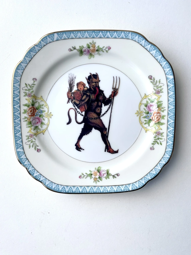 a naughty Christmas Krampus stealing a child, the image is victorian and is printed directly onto an ornate vintage plate