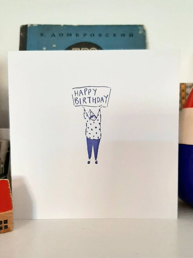 'Happy Birthday' Letterpress Handprinted Greetings Card, a white happy birthday card sitting on a white surface. It has a blue design. 