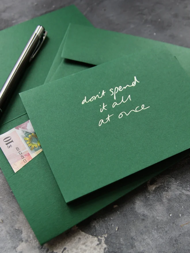 Hand foiled cash card or money wallet in a forest green colour handfoiled in shiny lime green text which says 'don;t spend it all at once'.