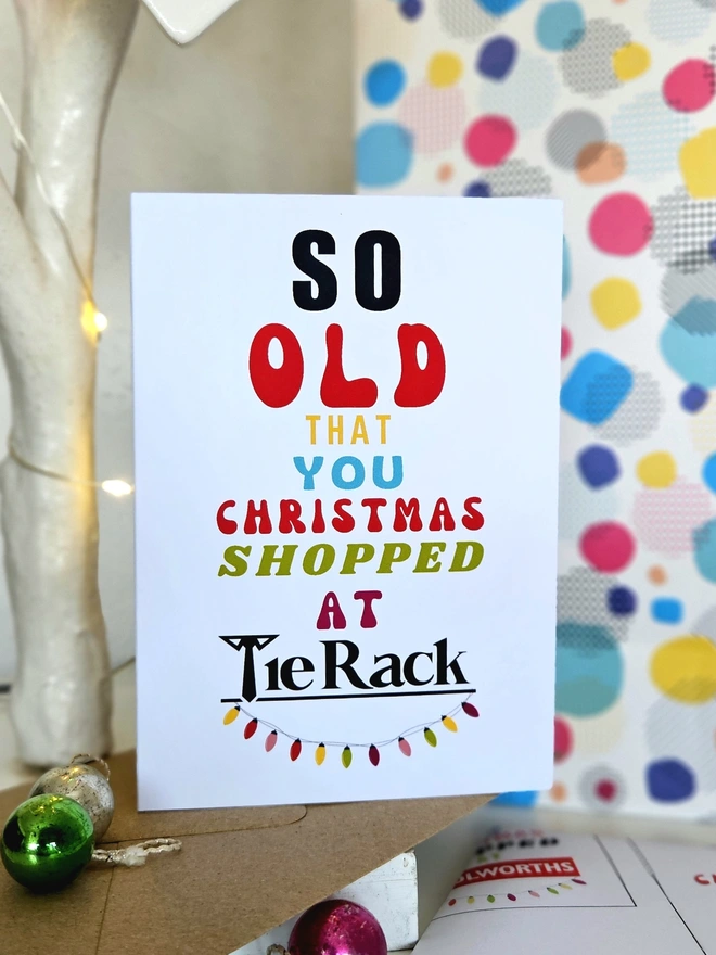 A photograph of the front of a humorous A6 greeting card illustrated using brightly coloured text and the retro shop logo. The text says so old  that you Christmas shopped at Tie Rack with string lights