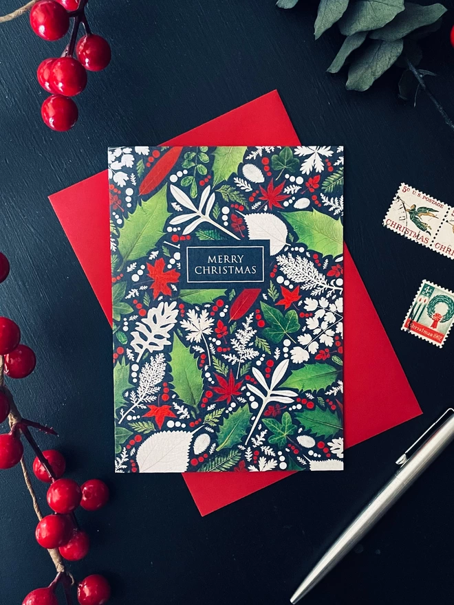 Christmas Card with Pressed Winter Leaf Design - Holly, Ivy - Dark Charcoal Coloured Desk - Red Envelope, Red Winter Berries, Vintage Stamps, Silver Pen