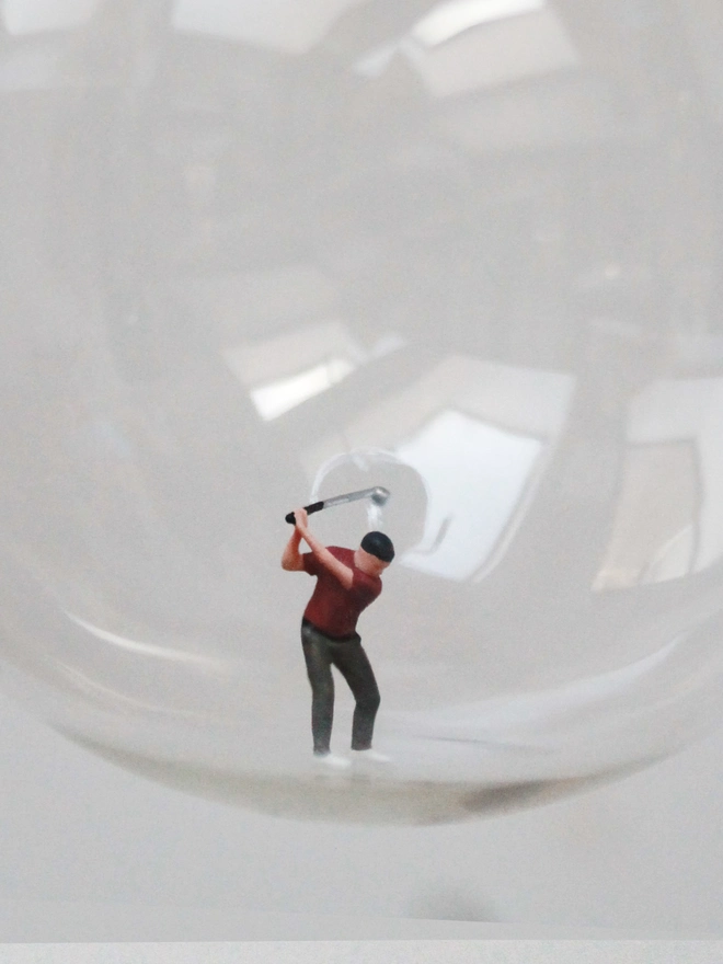 Miniature figure of a male golfer in a glass Christmas bauble - close up 