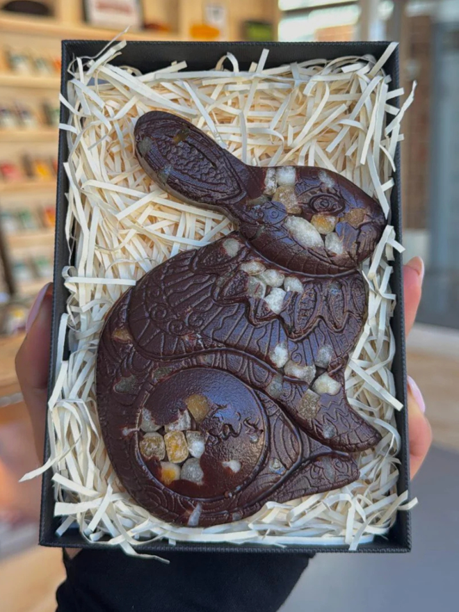 Sicilian Orange Vegan Chocolate Luigi Bunny being held up within a shop, in a box filled with straw