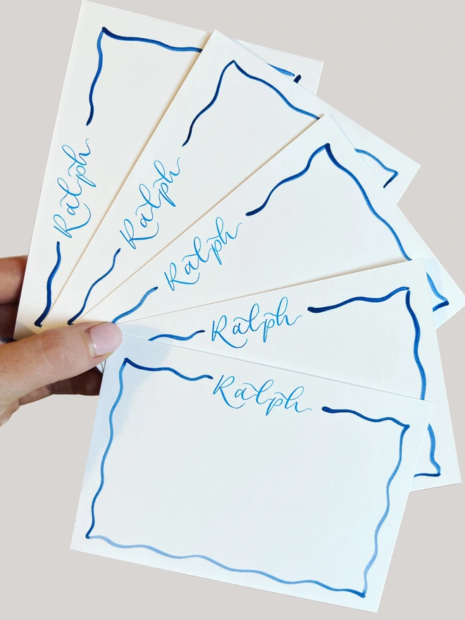 Five white notecards with Ralph handwritten in bright blue calligraphy at the top, and a darker blue wavy border around the edge of the card.