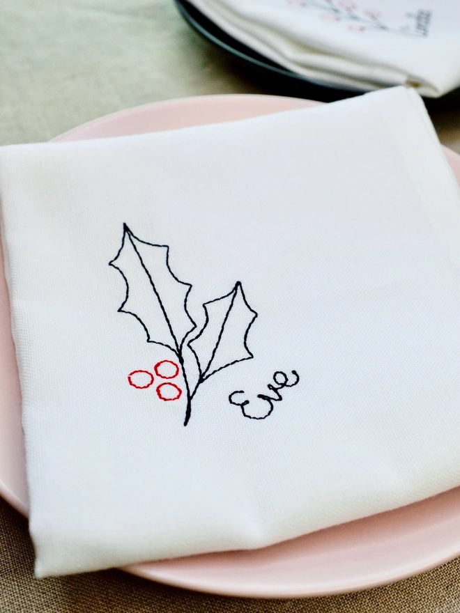 Holly embroidered napkin with custom name in black cursive text, cotton Christmas napkin