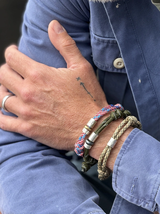 men's personalised drift paracord bracelet. a close up of a man's arm in a denim shirt wearing three different paracord bracelets.