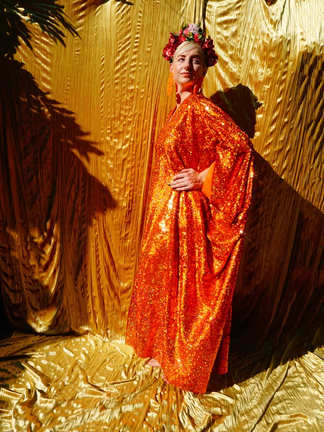 Woman wearing an Orange Sequin Kaftan dress seen with her hands on her hips.