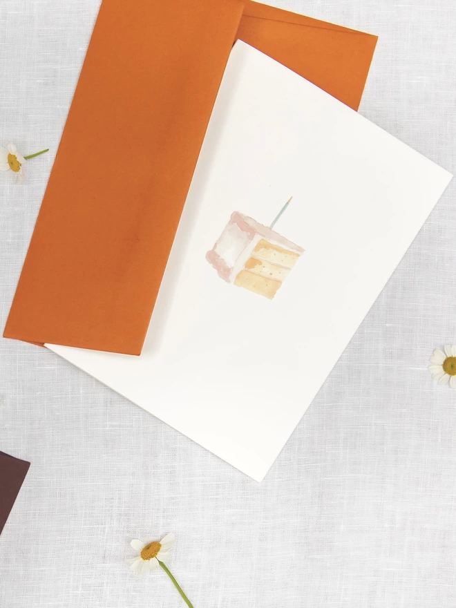 Greetings card with a watercolour illustration of a slice of birthday cake and a burnt orange russet coloured envelope