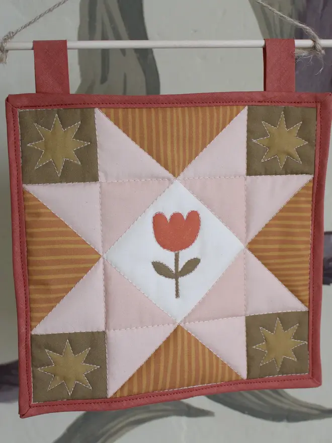 tulip quilt wall hanging. a patchwork quilt with a pink star pattern in the centre and embroidered tulip.