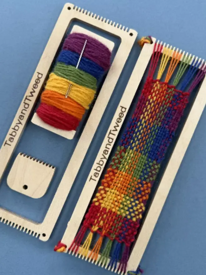Rectangular beige looms, one woven with bright rainbow coloured yarns with a spool of bright yarn and wooden comb.