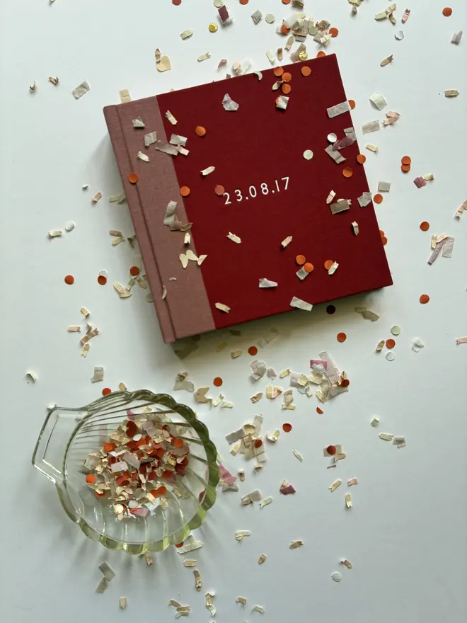 Confetti littered table with instant photo guest book by Keep Collect in Rose and Coral book cloth and personalised white foiled lettering