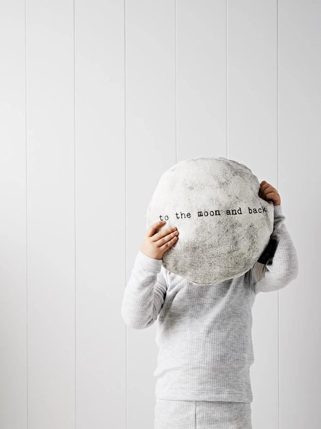Child holding moon shaped cushion with the words 'to the moon and back'