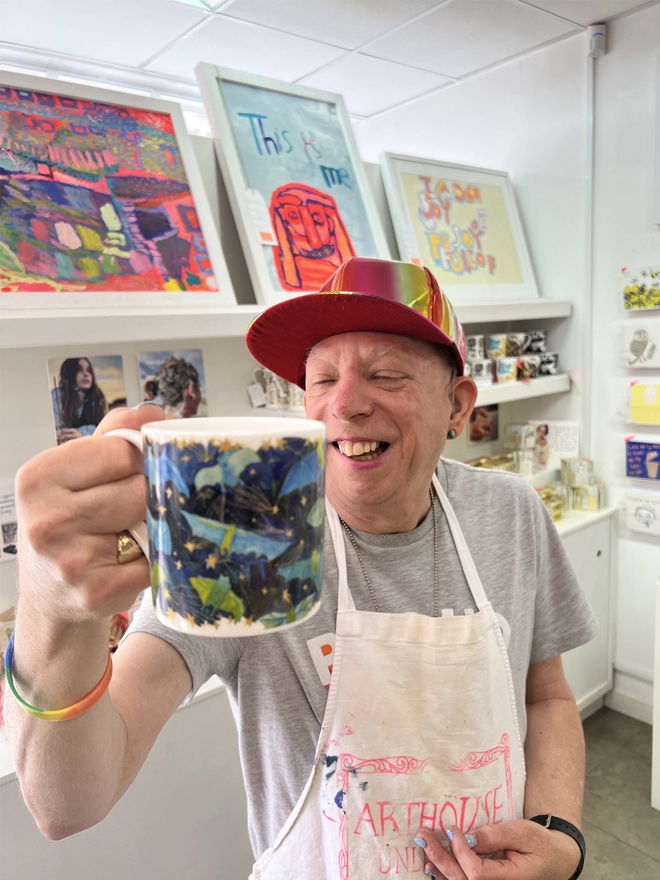 Happy artist holding bats fine bone china charity gift mug featuring gold, green & blue illustrations