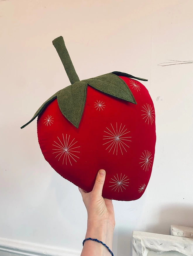 A red strawberry cushion being held against a white wall