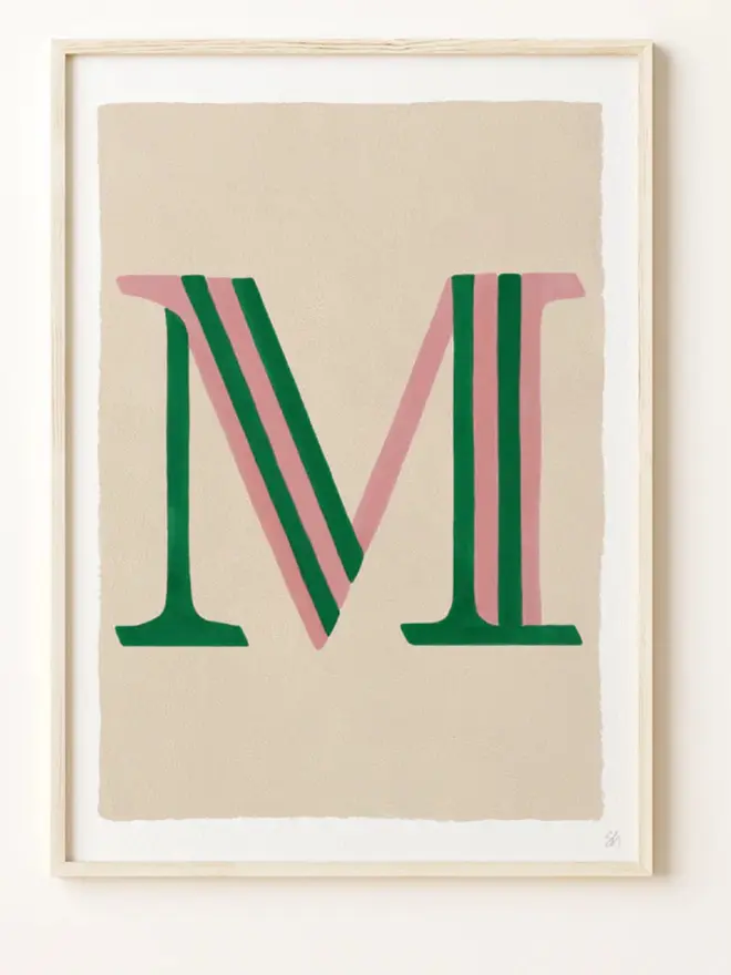 Framed wall art print featuring a large decorative letter “M” in humbug stripes
centered on a white background. 