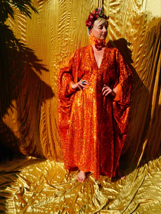 Woman wearing the Orange Holographic Sequin Kaftan seen with her hands on her hips.