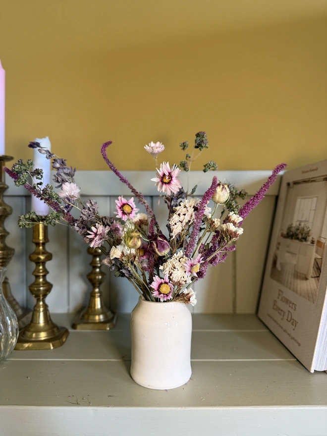 a selection of dried flowers in a ceramic vase on a shelf with candles in brass candlesticks