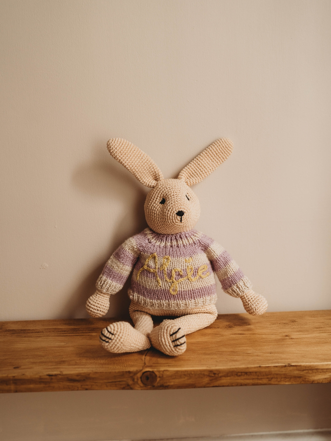 hand crochet bunny rabbit with personalised hand knit purple and white striped jumper on wooden shelf