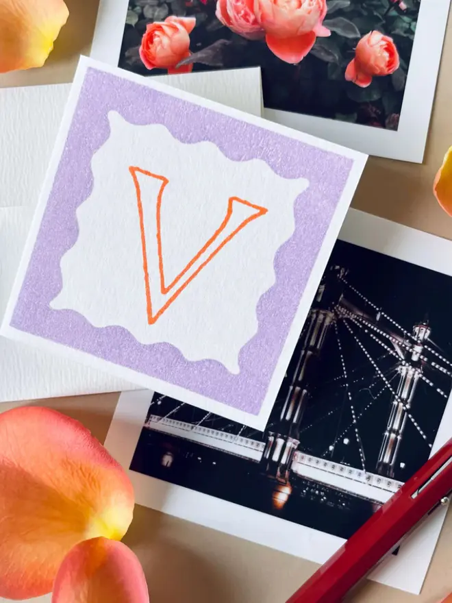 Hand-printed mini letter cards featuring an orange  “V” on a violet background, framed with scalloped edges.
