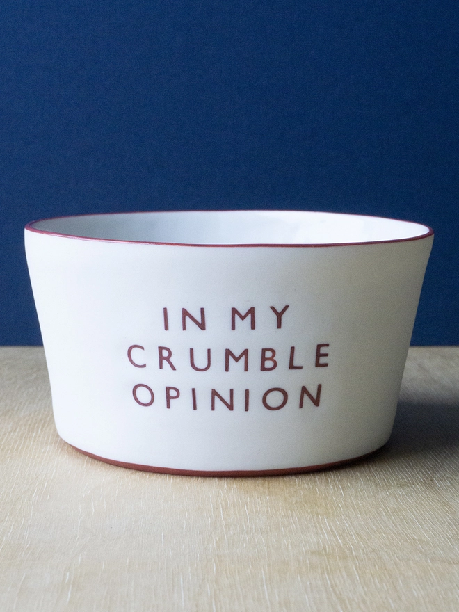Ceramic porcelain pudding bowl with In My Crumble Opinion written on the side. A white pudding bowl with red rim.