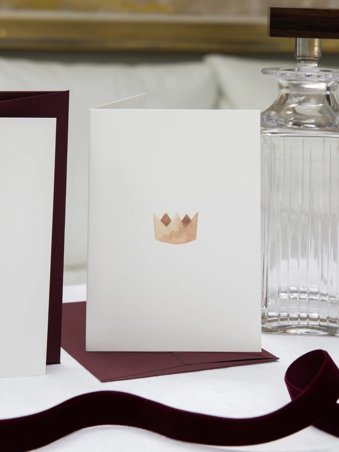 Greetings card with a watercolour illustration of a crown, with a burgundy grape envelope