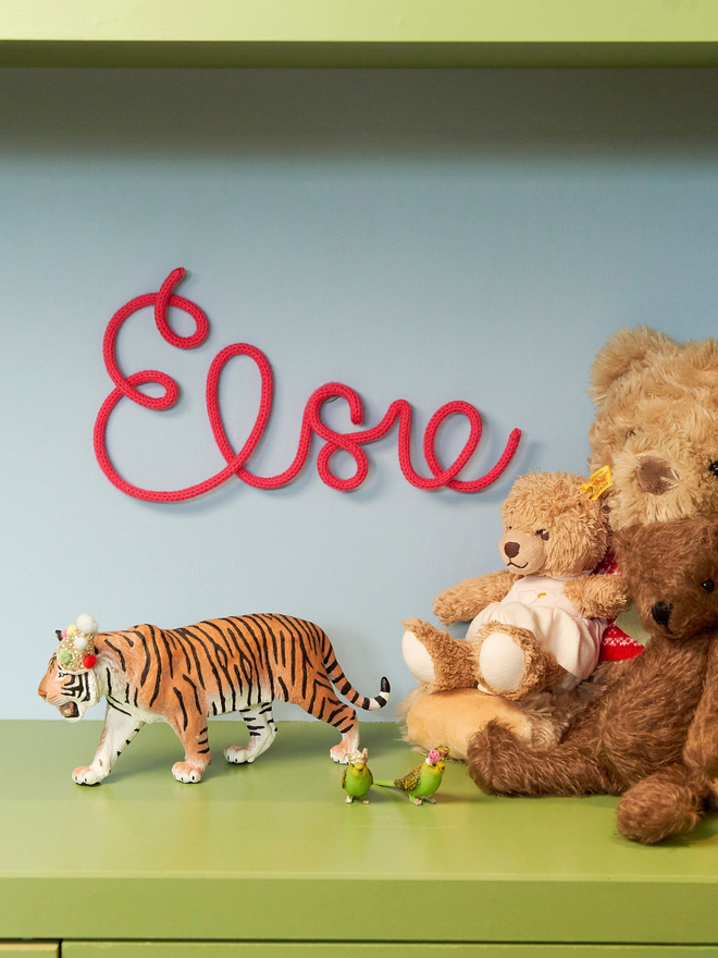 Personalised wire name knitted sign. Elsie written in red wire on a kids' room wall
