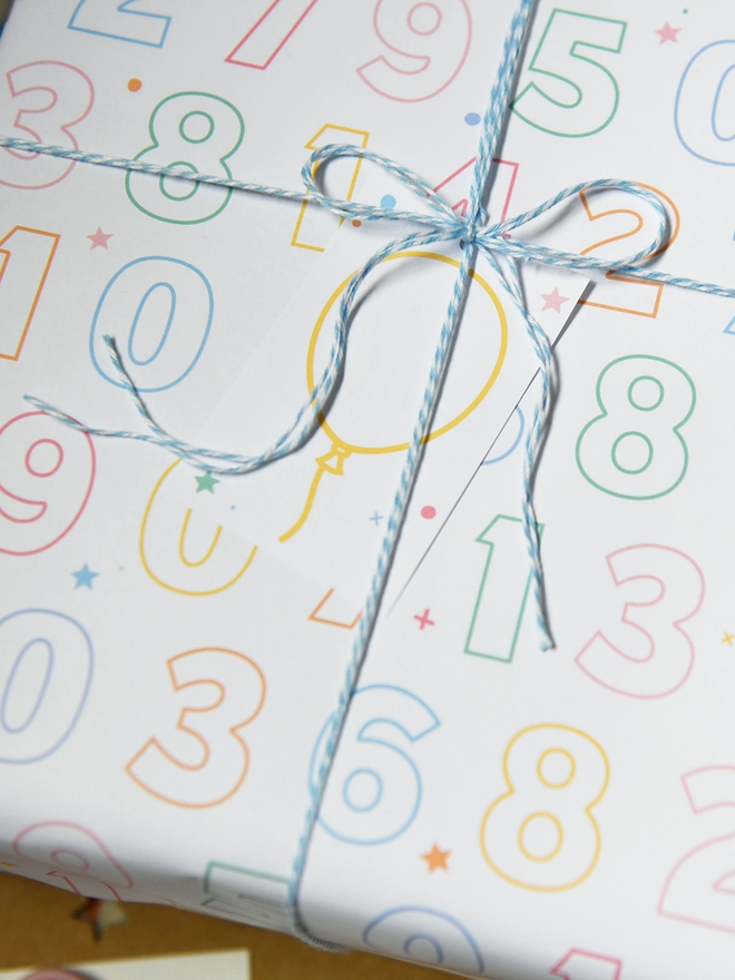 A birthday gift wrapped in colour-in numbers wrapping paper lays on a green rug.