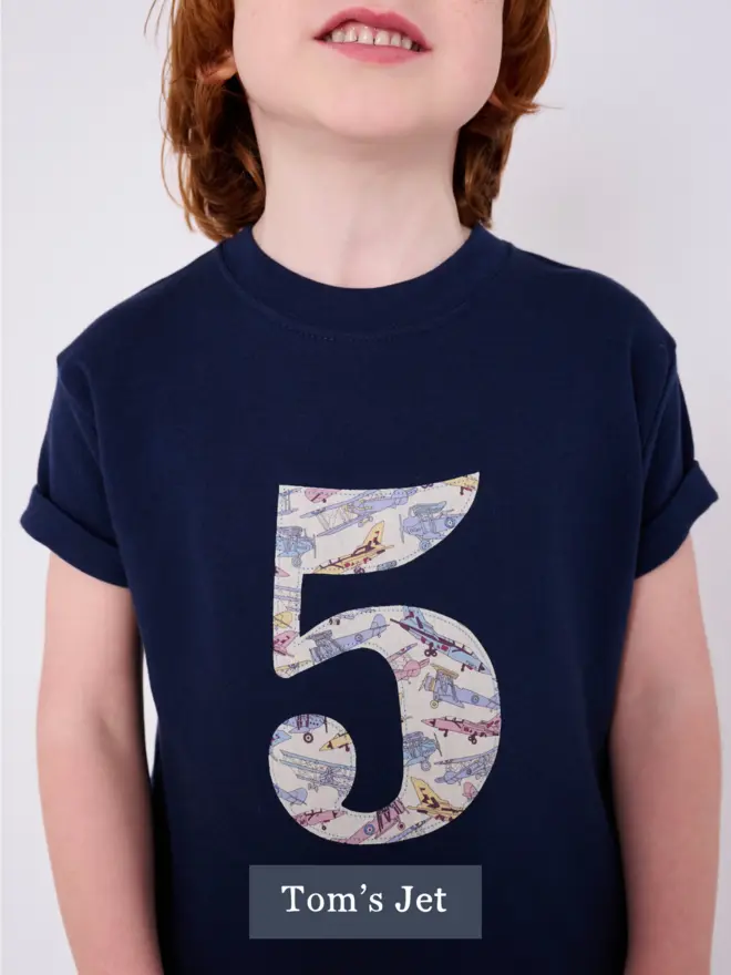 a 5 year old boy wearing a 5th birthday t-shirt with a number 5 on the front featuring vintage jet planes