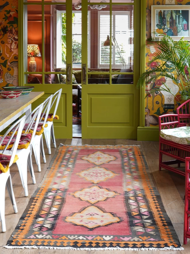 Orangey, red and black geometric vintage kilim hand woven rug on wooden floor in maximalist dining room with green woodwork