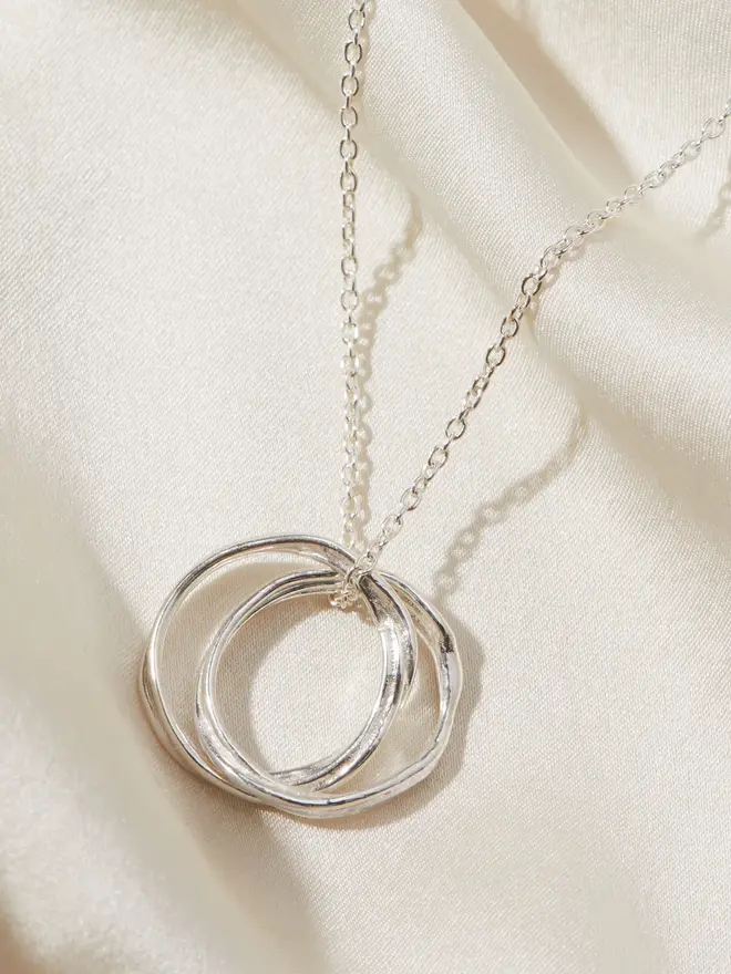 Close up image of the Silver Entwined Circles Necklace draped over a silk material