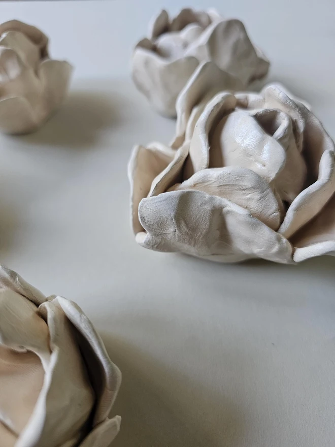 hand-sculpted ceramic flower in a soft cashmere glaze, featuring individually crafted petals and natural texture. Each unique piece is wall-mountable with a carved keyhole on the back