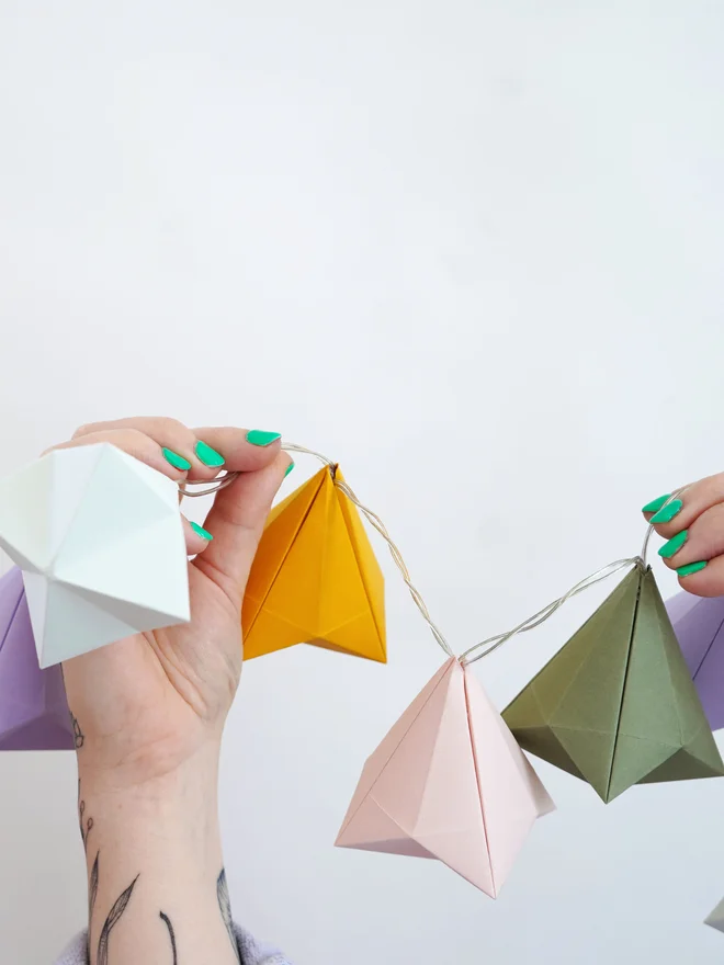 Woman's hands holding up a sting of colourful origami fairy lights