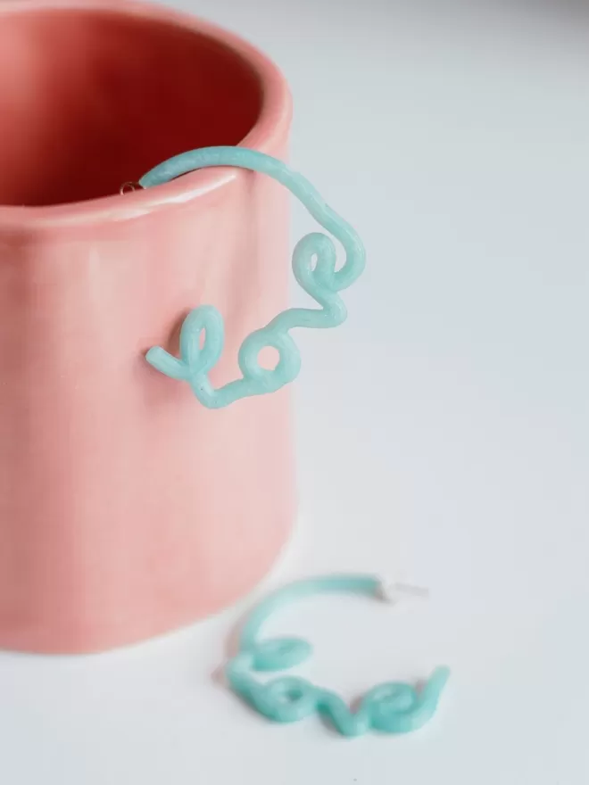 100% Recycled Ocean Plastic - 'Love' Hoop Earrings seen in a pink cup.