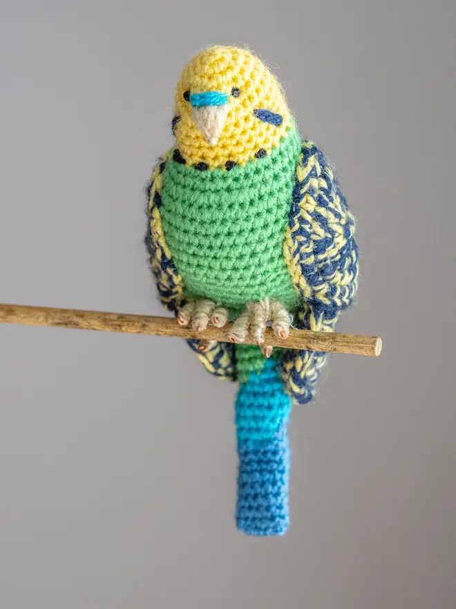 Budgerigar Hand Crocheted Figure, a green  crocheted bird sitting on a wooden poll. 