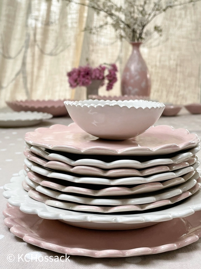 a stack of pink and white side dessert breakfast plates on a table setting with vases and flowers in background