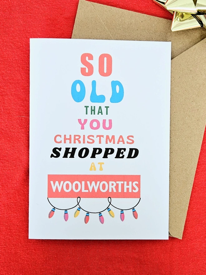 A photograph of the front of a humorous A6 greeting card illustrated using brightly coloured text and the retro shop logo. The text says so old you Christmas shopped at Woolworths with a colourful string of looped fairy lights.