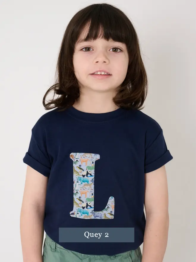 a 4 year old boy wearing a personalised navy t-shirt with his initial cut from liberty print featuring zoo animals