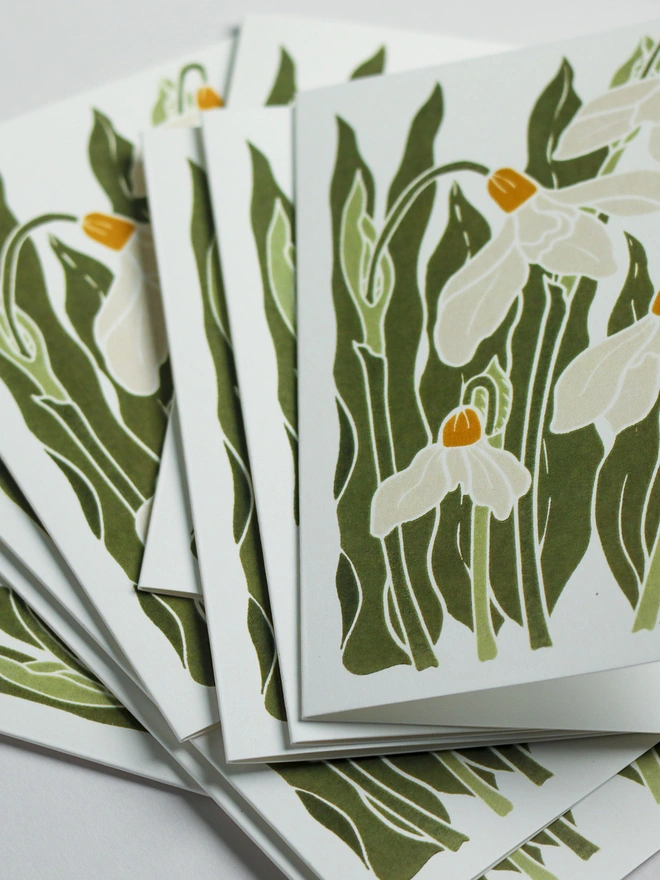 Set of 8 hand-carved botanical notecards featuring snowdrops in the garden. A6 linocut print greeting cards in classic cream and green, displayed with kraft envelopes. Cottagecore stationery on recycled cardstock.