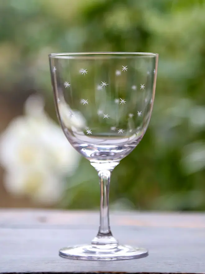 engraved stars crystal wine glass. a crystal wine glass with star details on an outside table.