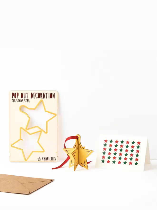Pop out star hanging Christmas decoration with red ribbon for hanging and star repeat pattern Christmas card and brown kraft envelope on a white background