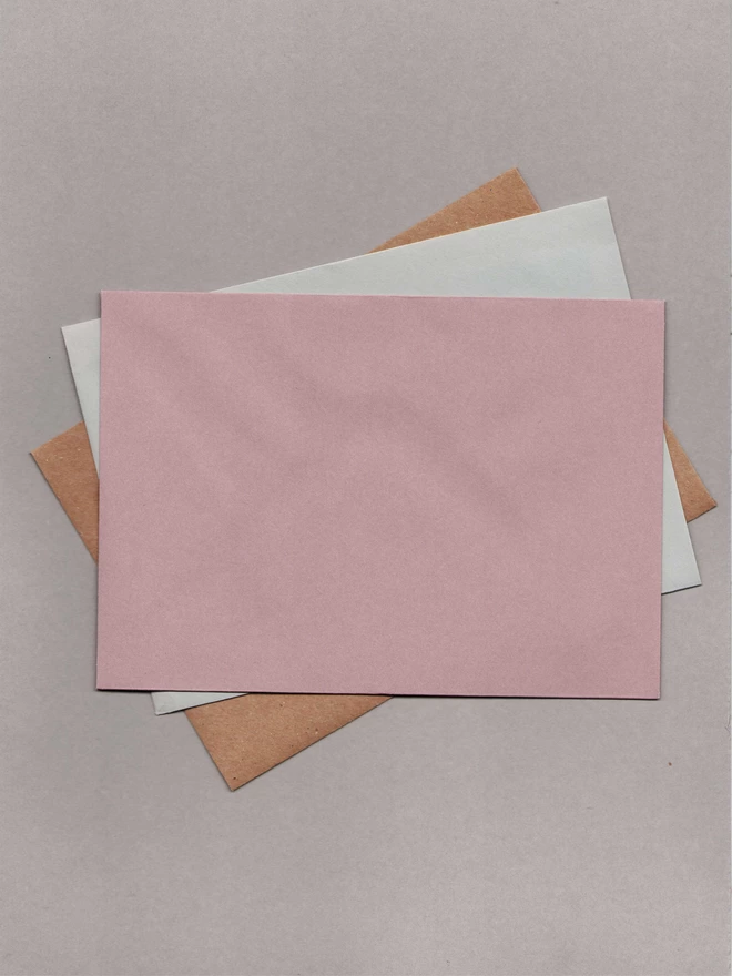 Three envelopes laid out on top of each other. The top one is mulberry, the second is grey and the bottom is kraft paper.