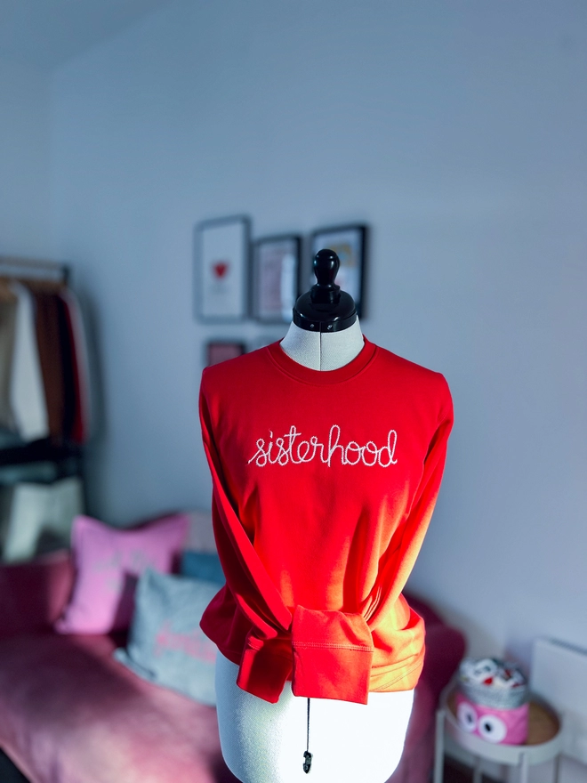 A dressmakers dummy with a red sweatshirt embroidered sisterhood