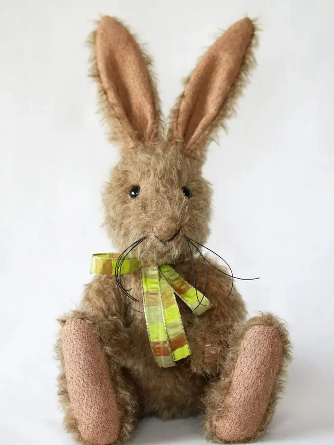 Handmade brown stuffed rabbit with long ears and a green ribbon bow sitting upright against a plain background.