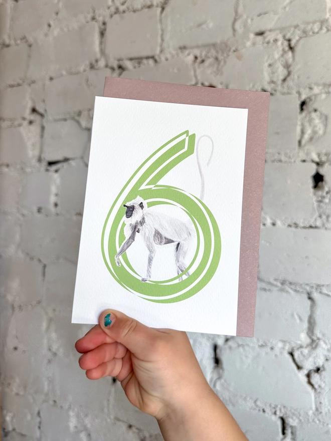 white card with a big green number 6 and an illustrated monkey with a purple envelope
